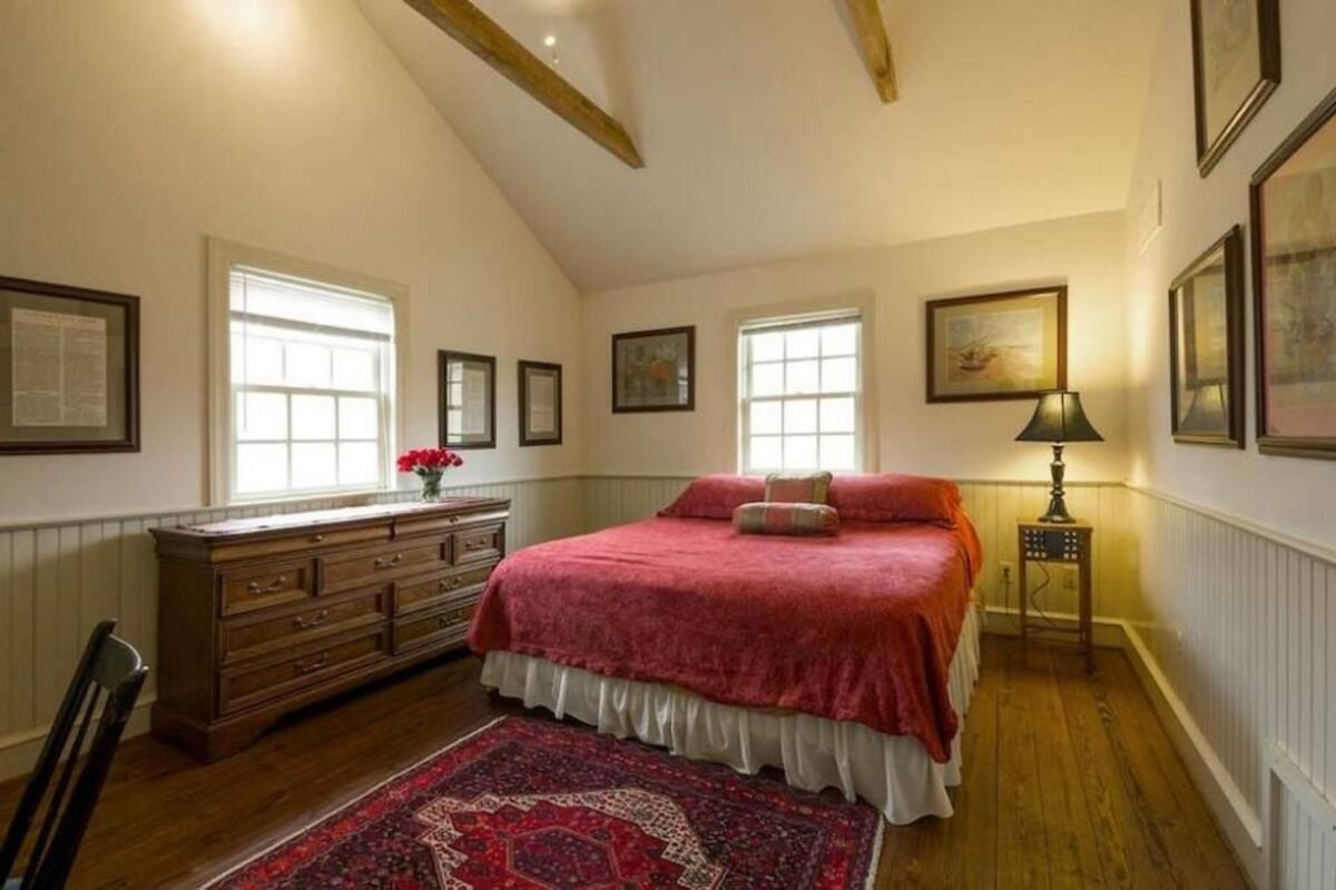 A bedroom with a large bed, wooden dresser, and a red rug.