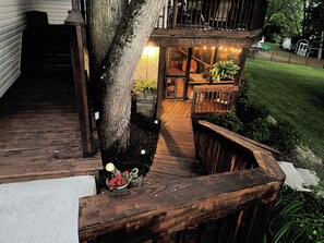A wooden deck with a built-in bench and a small table, surrounded by greenery and a white fence. - Amish Country Comfort (Millersburg)