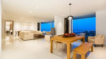 Una sala de estar moderna con una mesa de comedor de madera, sofás color beige y un ventanal con vistas a la ciudad.