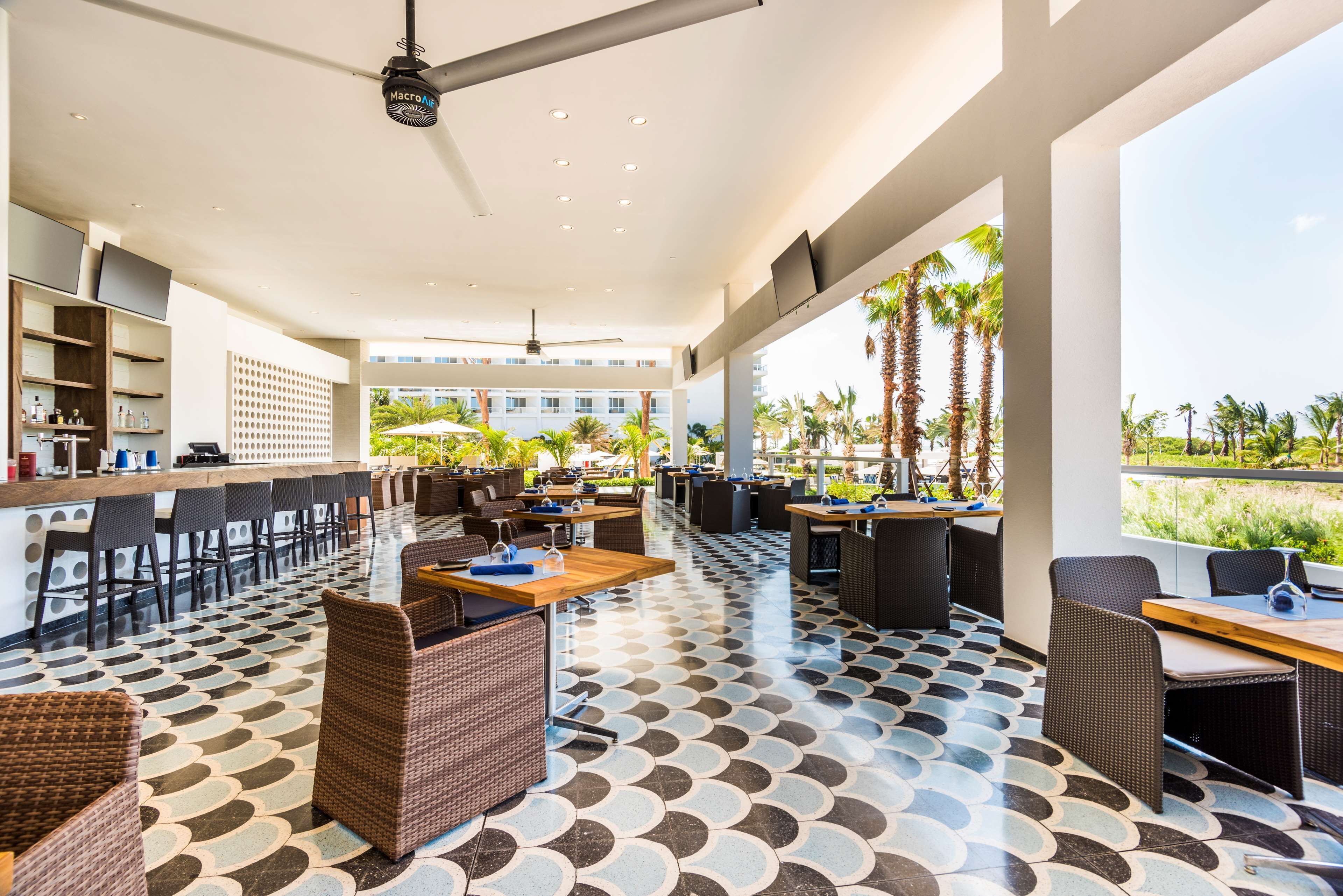 A spacious outdoor lounge area with a long counter, multiple seating arrangements, and a patterned floor.