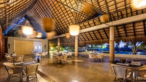 A spacious outdoor dining area with thatched roof, wicker furniture, and a view of the pool and palm trees.