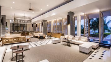 Eine großzügige Lobby mit modernem Design, ausgestattet mit einer großen Sitzecke, einem Empfangsbereich und Blick auf Palmen.