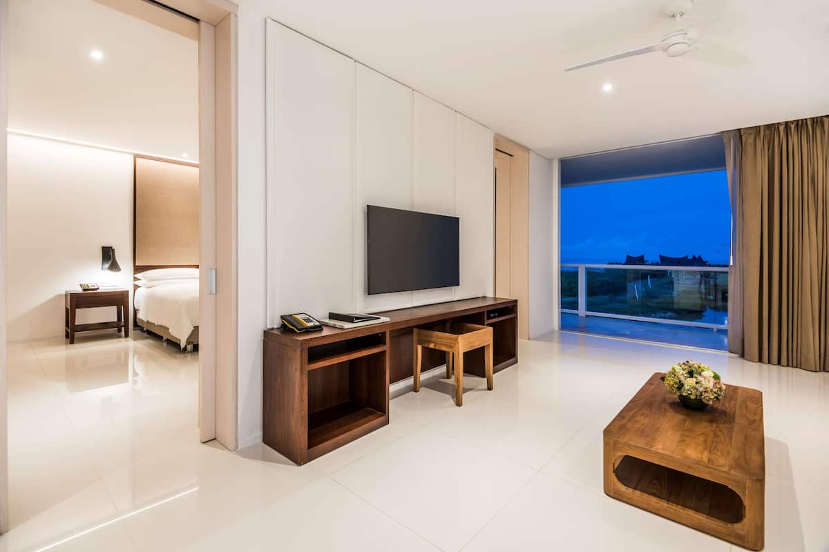 Une chambre d’hôtel moderne dotée d’un grand téléviseur à écran plat, d’un meuble de rangement en bois et d’un balcon avec vue.