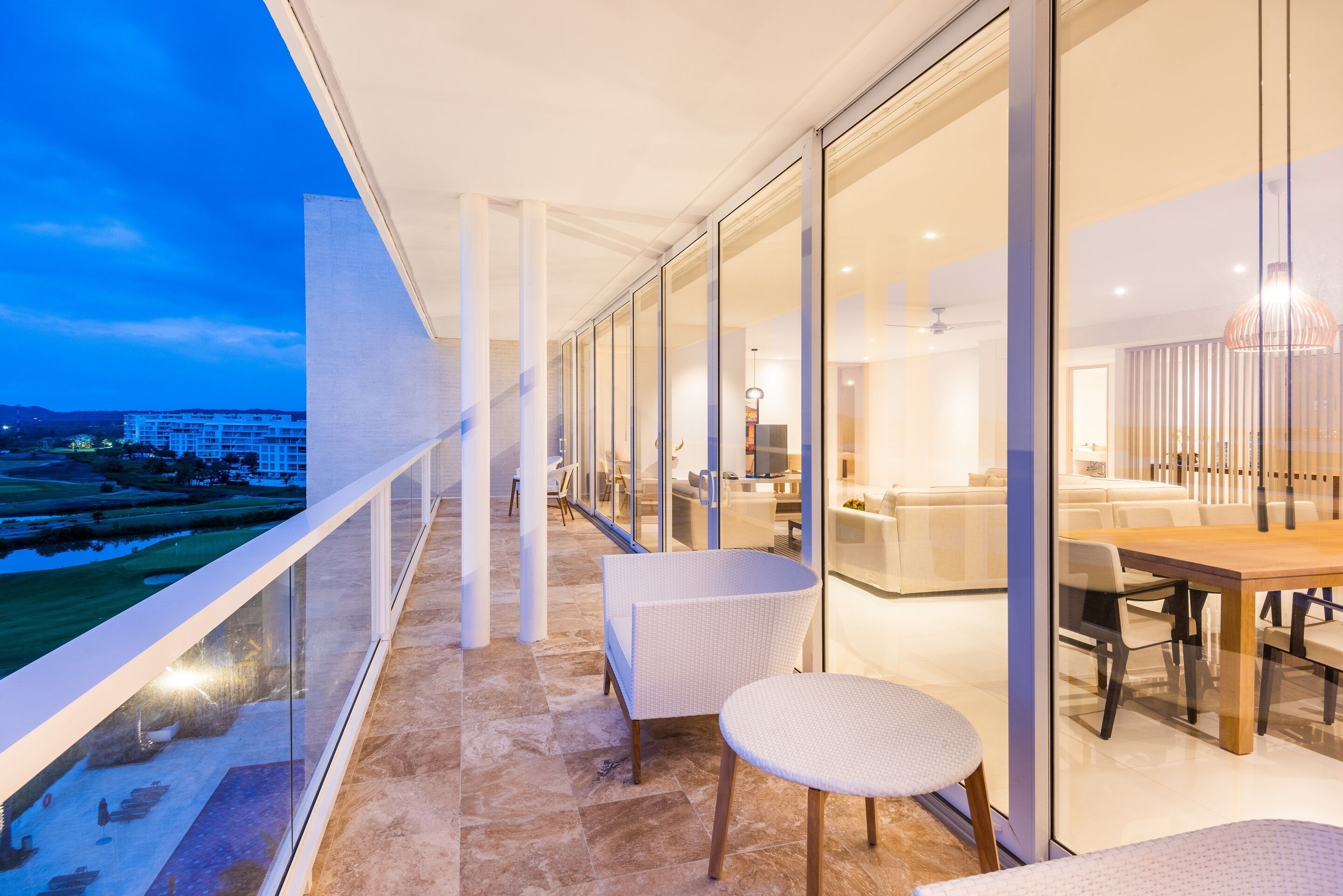 Un balcón de hotel moderno con puertas de cristal, una zona de comedor con mesa y sillas, y vistas a un campo de golf.