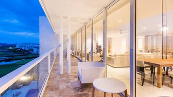 A modern hotel balcony with glass doors, a dining area with a table and chairs, and a view of a golf course.