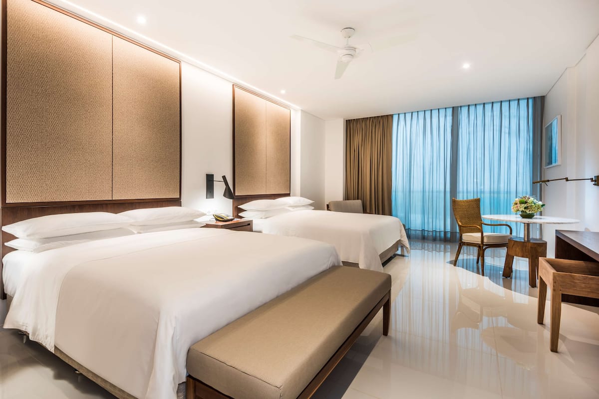 Une chambre d’hôtel avec deux lits, un banc, un bureau et une chaise.