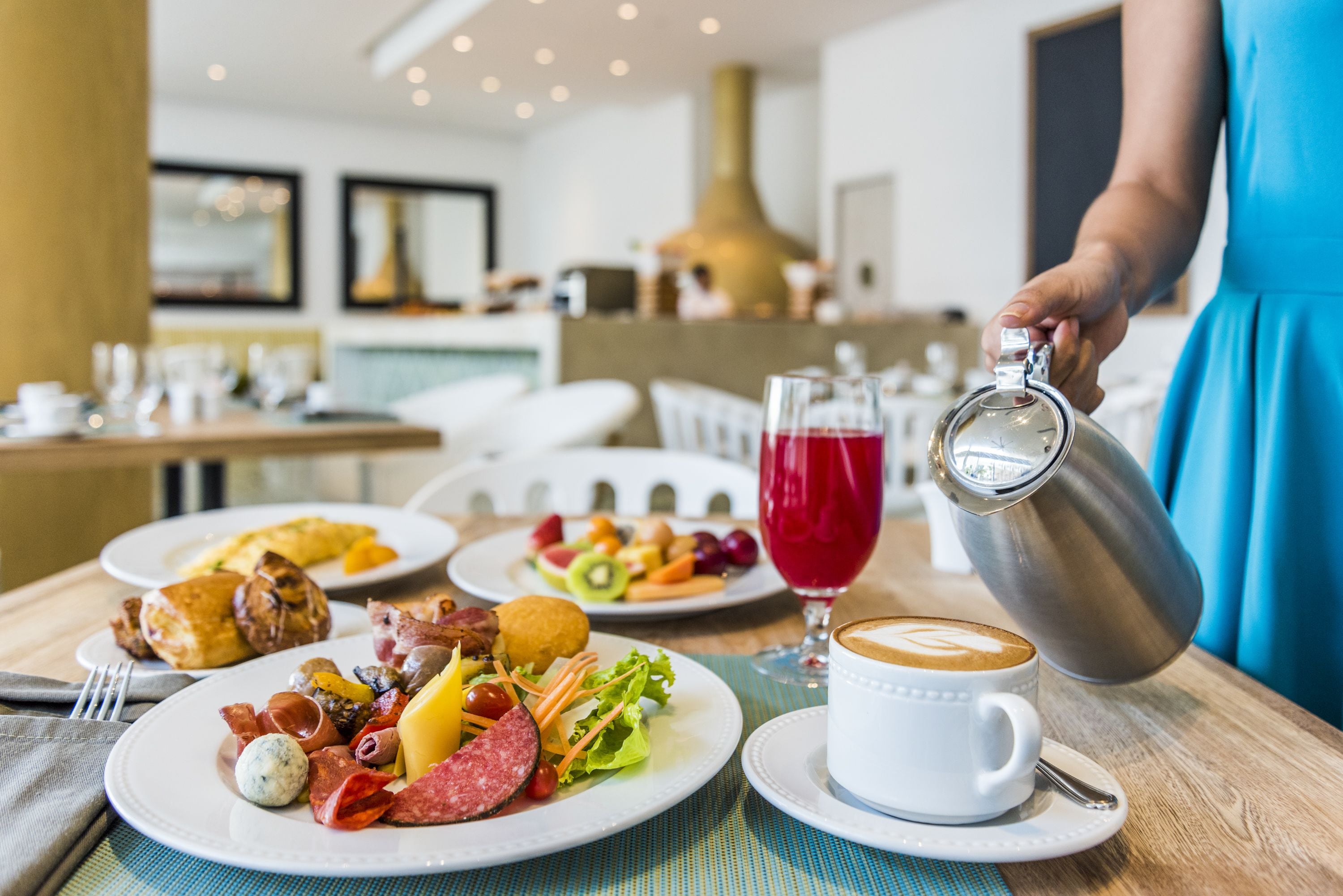 A breakfast setting with plates of food, a coffee cup, and a person pouring a drink.