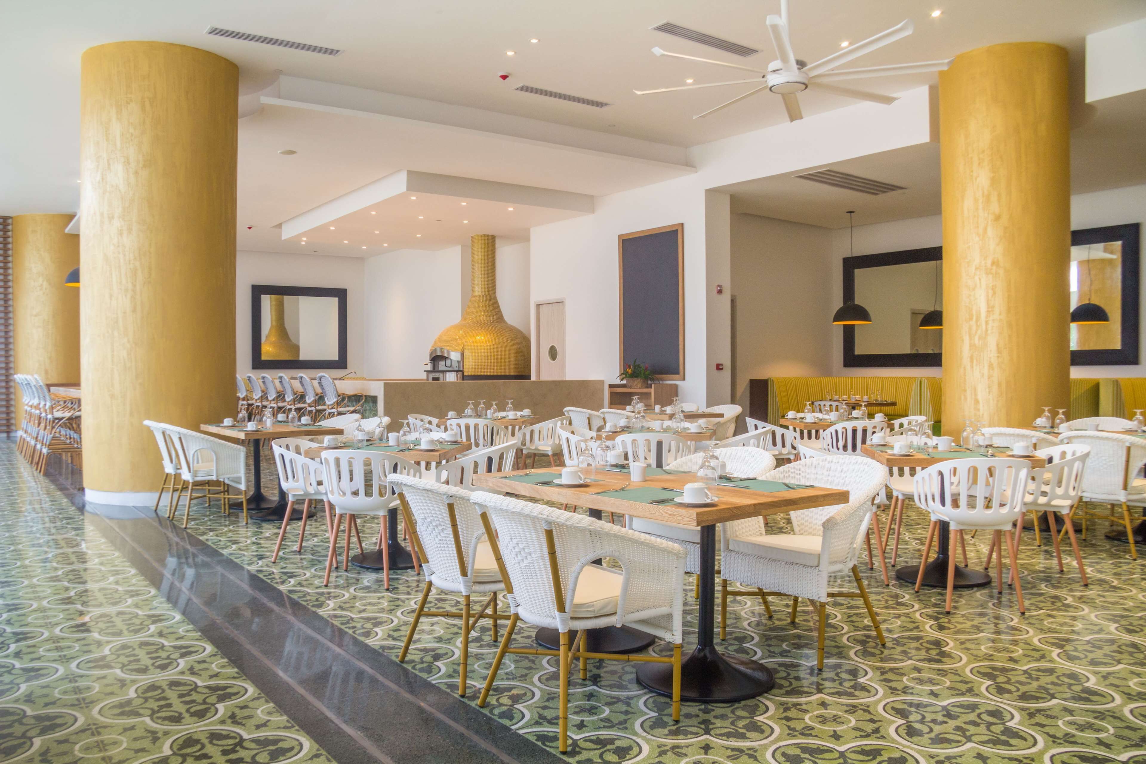 A spacious dining area with multiple tables and chairs, large golden pillars, and a patterned floor.