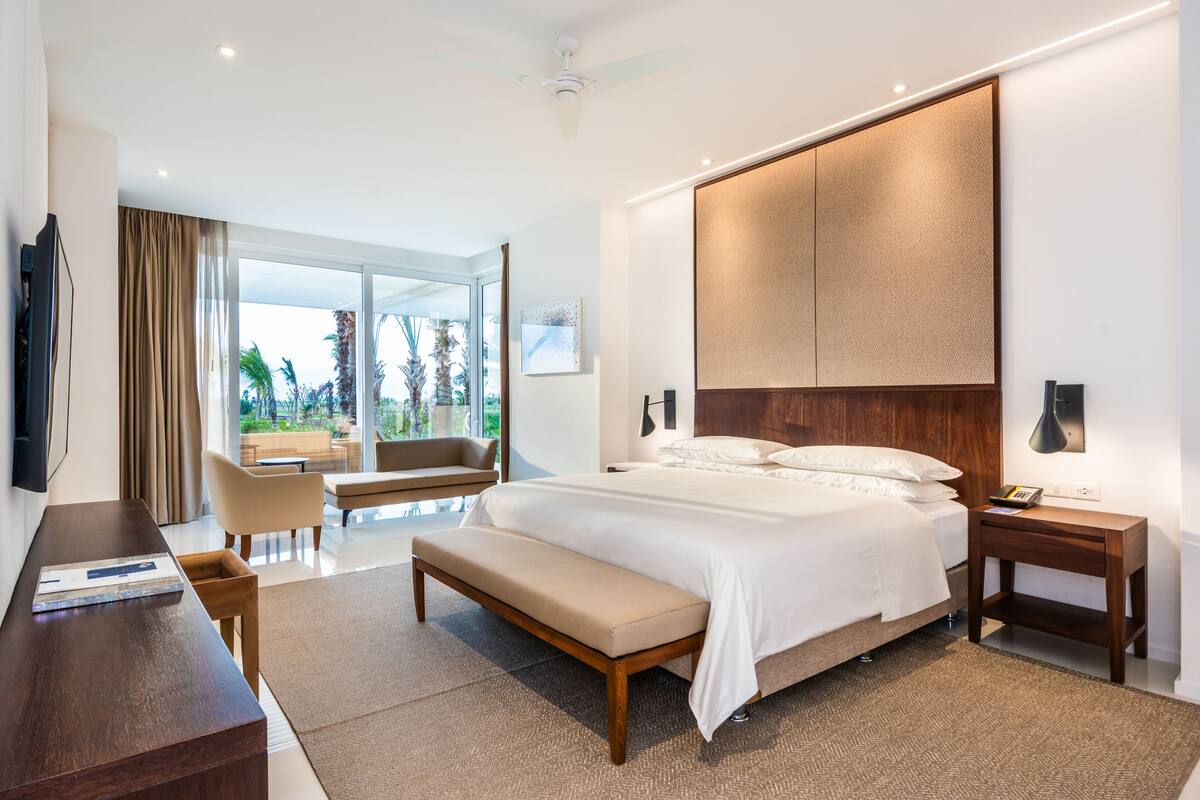 Une chambre à coucher moderne avec un grand lit, une table de chevet, un banc, un bureau et un téléviseur.