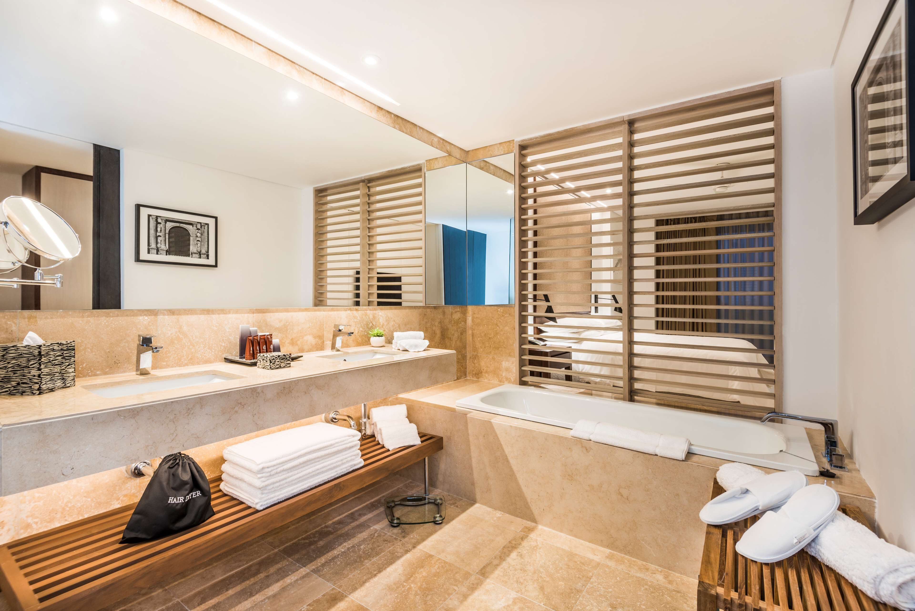 Un baño moderno con dos lavamanos, un espejo grande, persianas de madera, una bañera y toallas ordenadas.