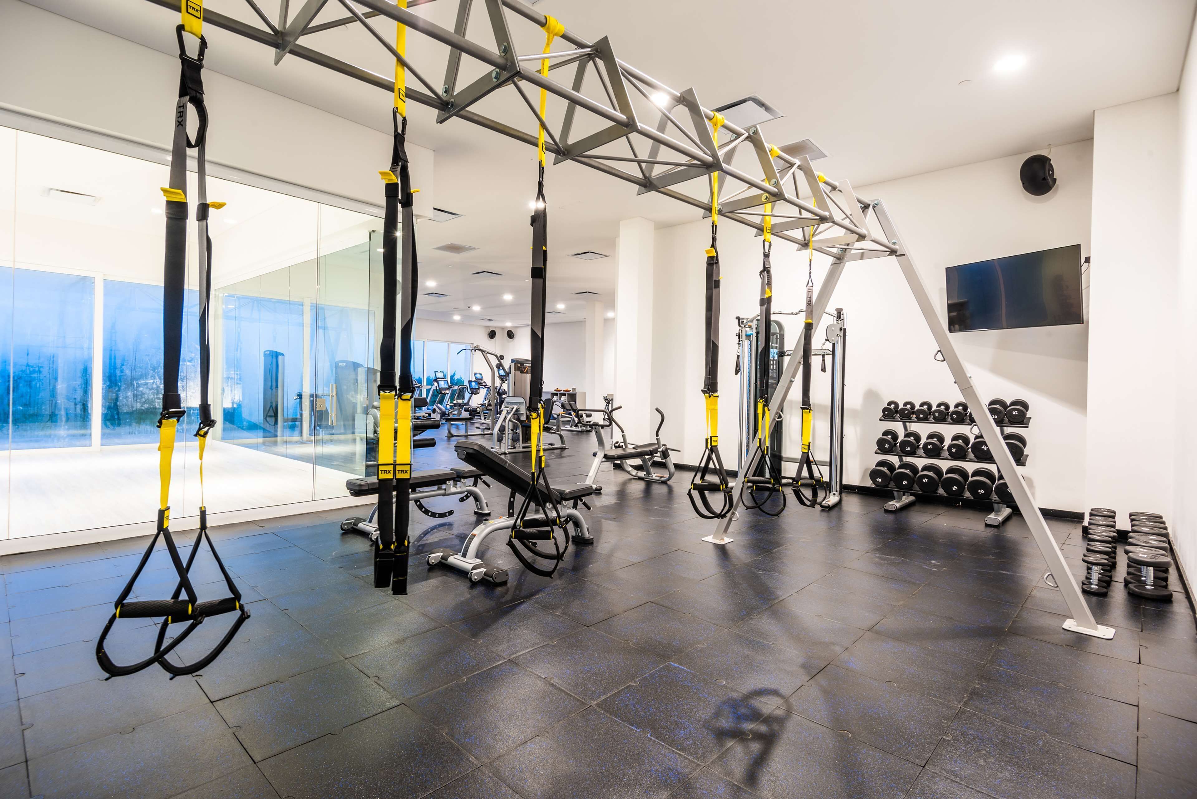 A modern gym with suspended training equipment, exercise bikes, and a wall-mounted TV.
