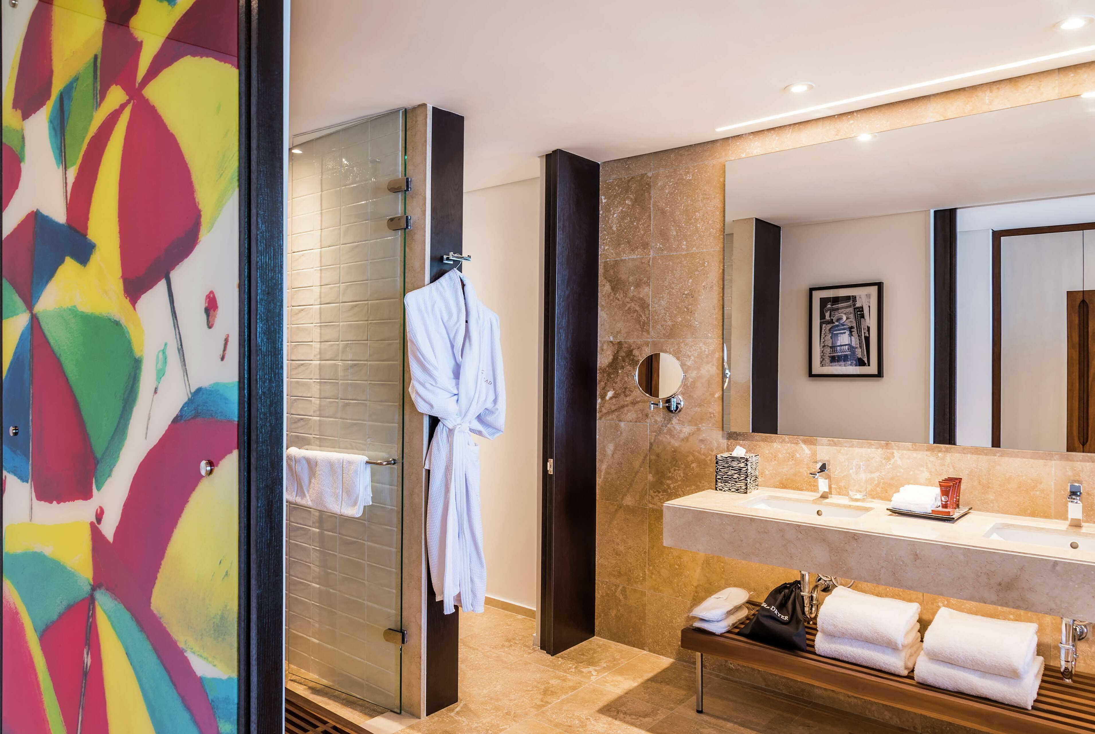 A modern bathroom with a glass shower enclosure, a large mirror, a vanity with a sink, and a bench with towels.