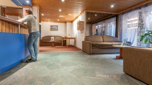 A hotel lobby with a wooden ceiling, stone flooring, a reception desk, a brown sofa, and a dining table with chairs. - Maeva Particuliers - Résidence Les Ravines (Les Allues)