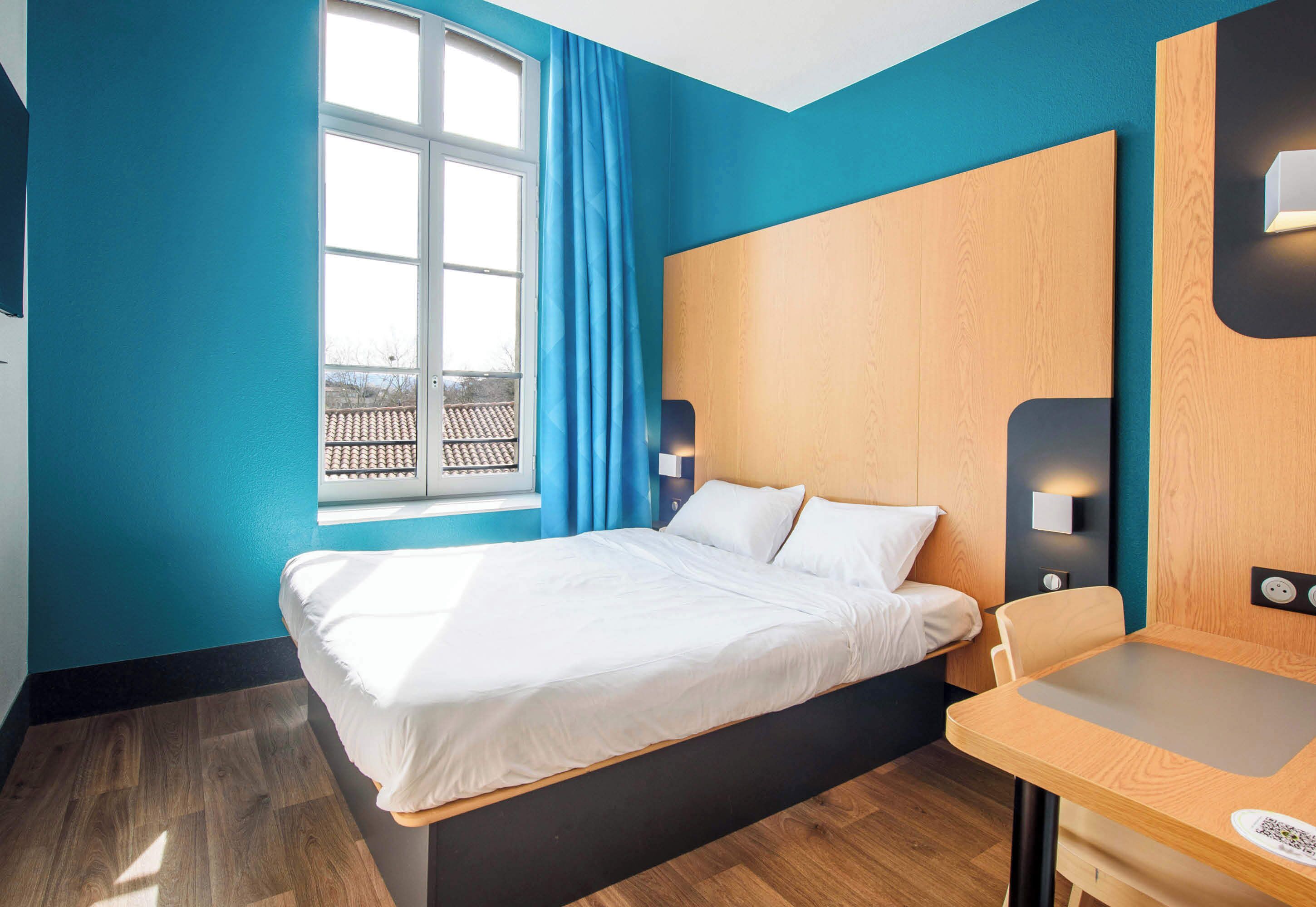 Una habitación de hotel moderna con cama, escritorio, ventana con cortinas y vista al exterior.