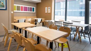 Un comedor con varias mesas y sillas, un ventanal con vistas al exterior y una pared con paneles de colores y fotografías enmarcadas.