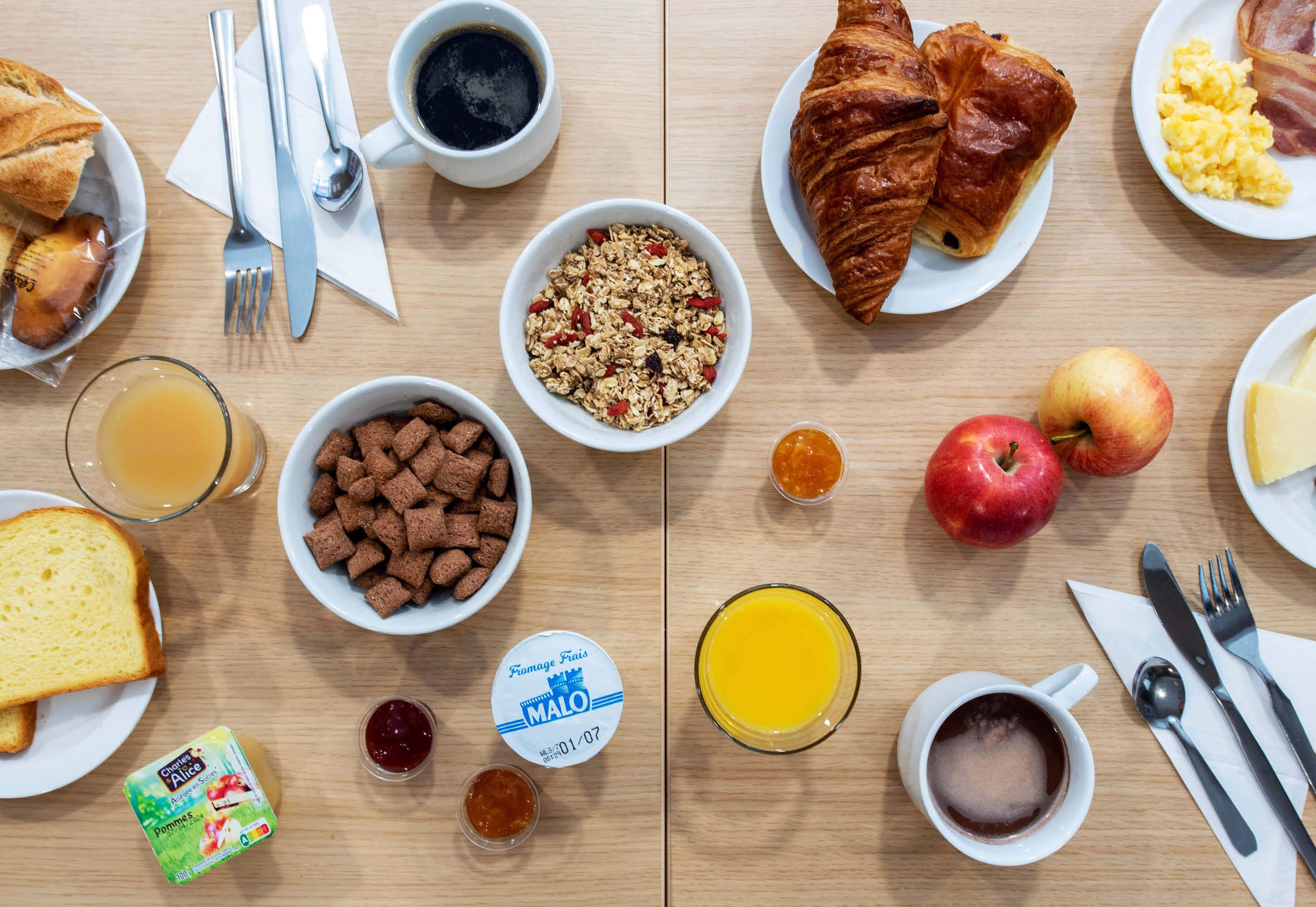 A breakfast table with croissants, cereal, fruit, and beverages.