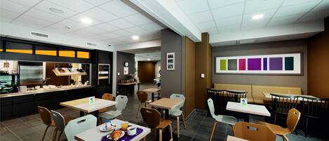 A modern dining area with tables and chairs, a kitchen in the background, and a wall with color samples.