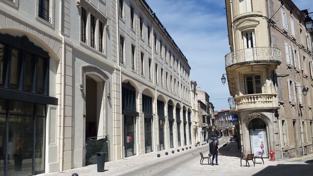 A street with historic buildings, including a building with a balcony and a sign for 'AXA'. - B&B HOTEL Castres Centre Gambetta (Castres)