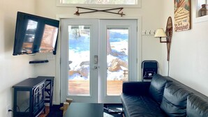 A living room with a television, a black leather sofa, a wooden table, and a door leading to a snowy outdoor area. - Lawson Adventure Park (Idaho Springs)