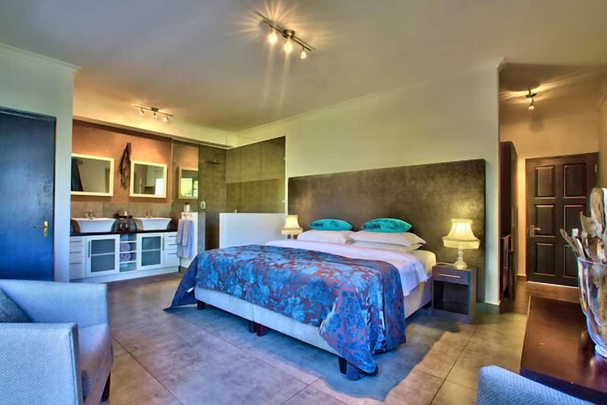 Un dormitorio moderno con una cama grande, mesitas de noche, un armario empotrado y un baño con tocador y espejo.