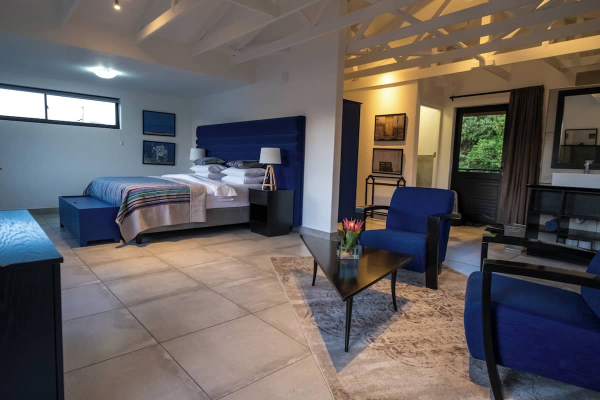 Una habitación de hotel moderna con cama, escritorio, silla, sofá y baño visible a través de una puerta abierta.