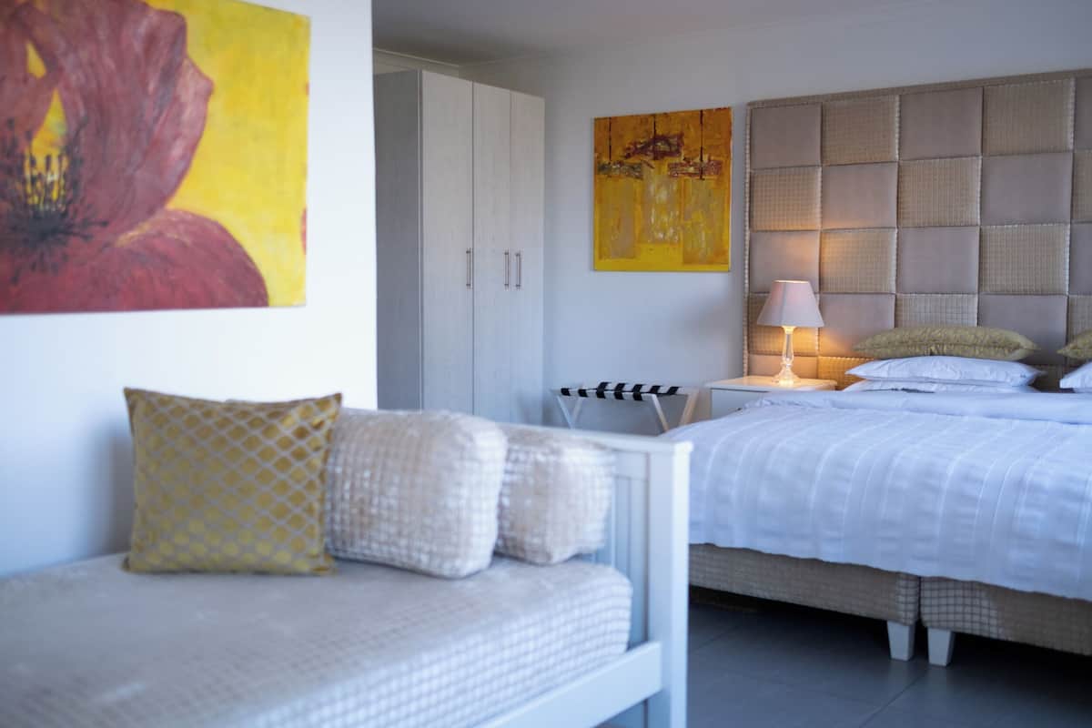 Un dormitorio con cama, una mesita de noche con lámpara, un sofá con cojines, un armario y dos cuadros en la pared.