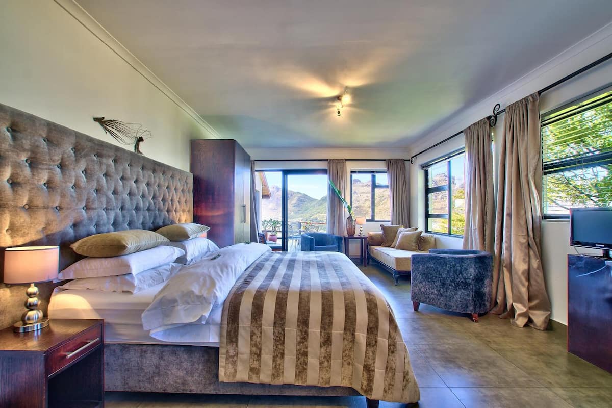 Habitación de hotel con una cama grande, un sofá, un televisor y vistas a las montañas.