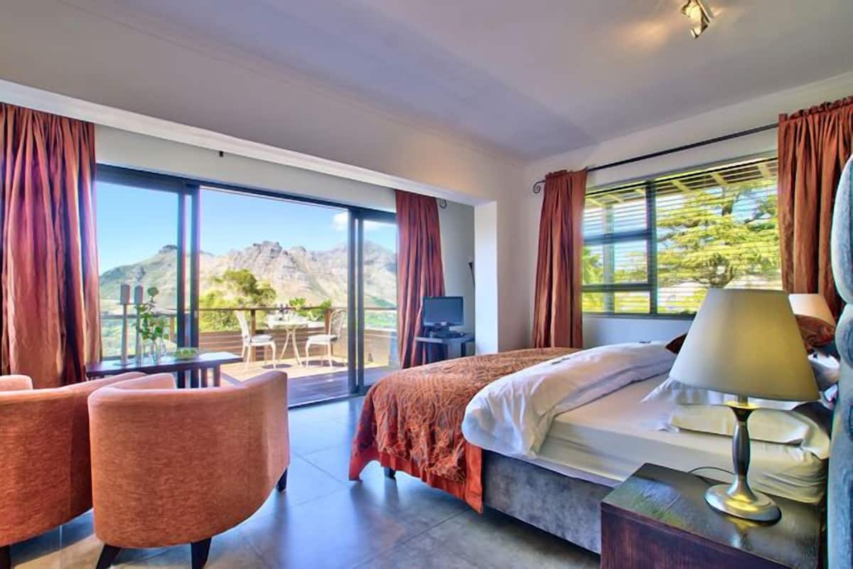 Habitación de hotel con cama, escritorio, silla y ventanas amplias con vista a la montaña.