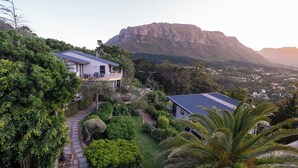 A residential property with a pathway leading to a house, surrounded by lush greenery and a prominent mountain in the background.