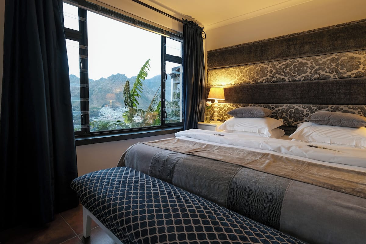Habitación de hotel con una cama grande, un banco, vistas a montañas y un cabecero con estampado.