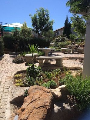Un patio con senderos de piedra, una fuente y diversas plantas.