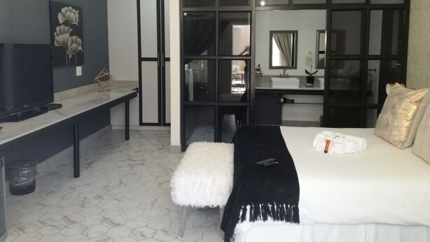 Una habitación de hotel moderna con una cama grande, un escritorio, un televisor y un vestidor.