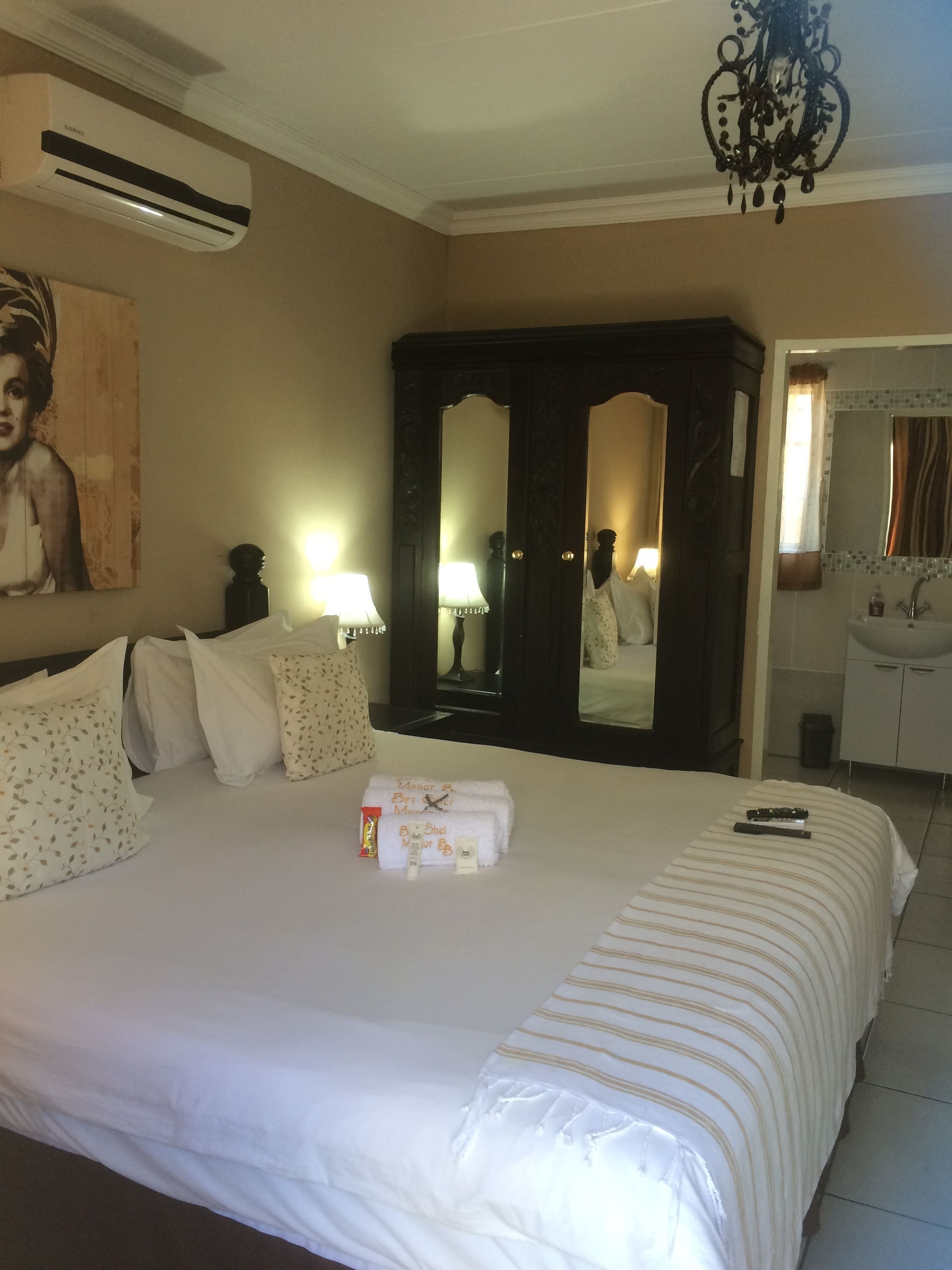 A hotel room with a large bed, a wardrobe, a mirror, a bathroom with a sink, and an air conditioning unit.