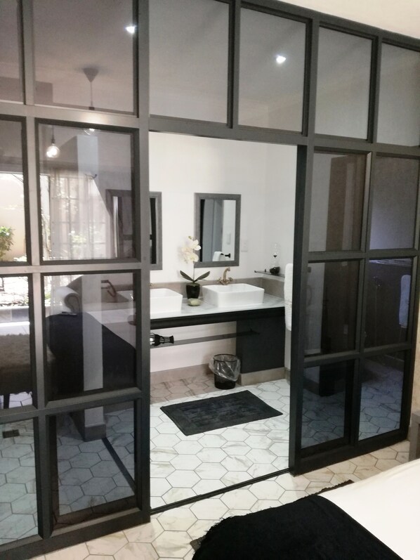 Une salle de bain moderne avec un grand miroir, un lavabo blanc et des carreaux de sol noirs.