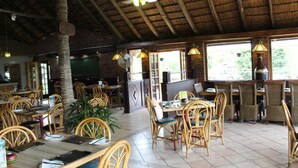 Un restaurant avec des tables et des chaises en bois, un toit de chaume et de grandes fenêtres.