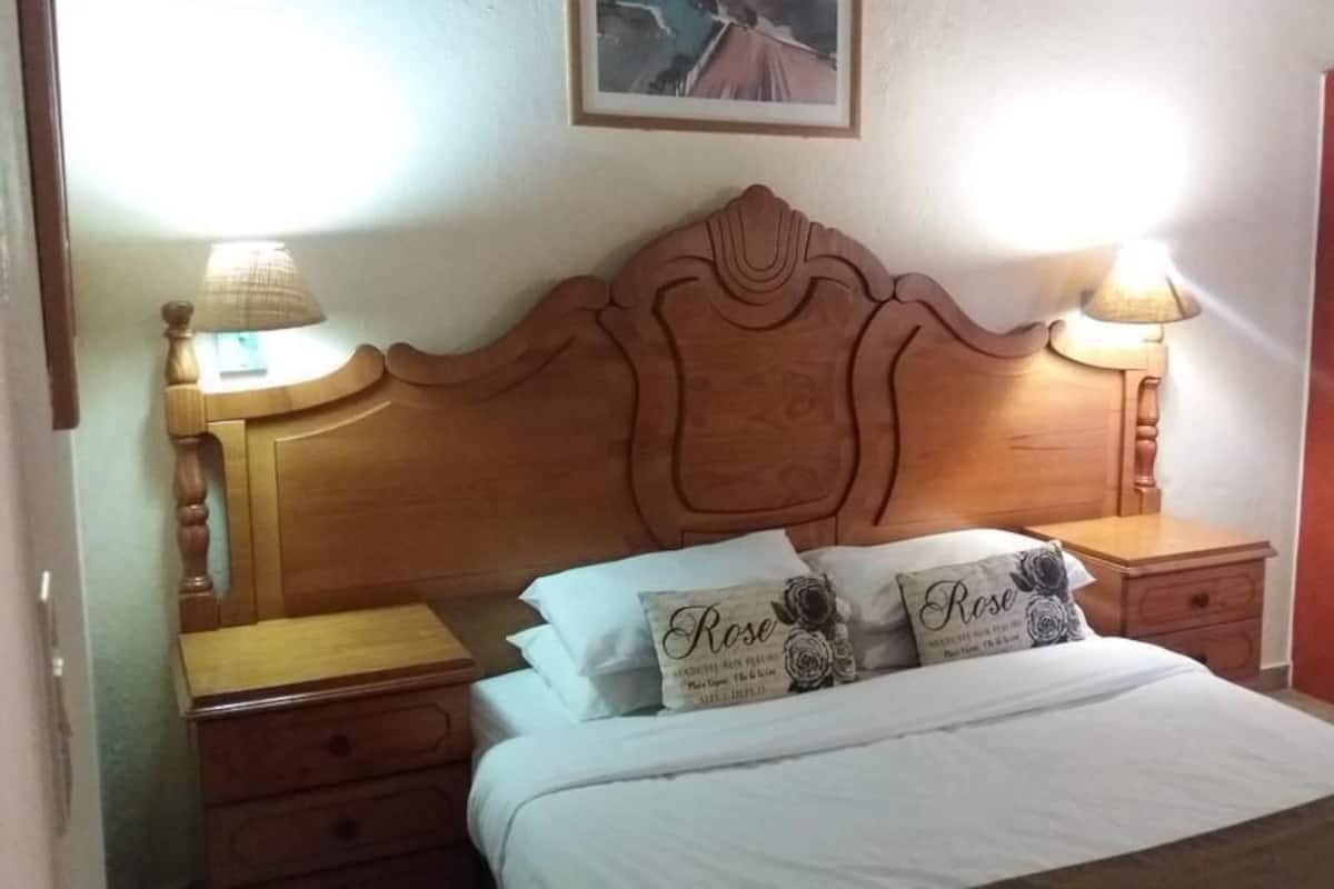 Een slaapkamer met een houten hoofdeinde, twee nachtkastjes met lampen, een bed met witte beddengoed en een rode garderobe.