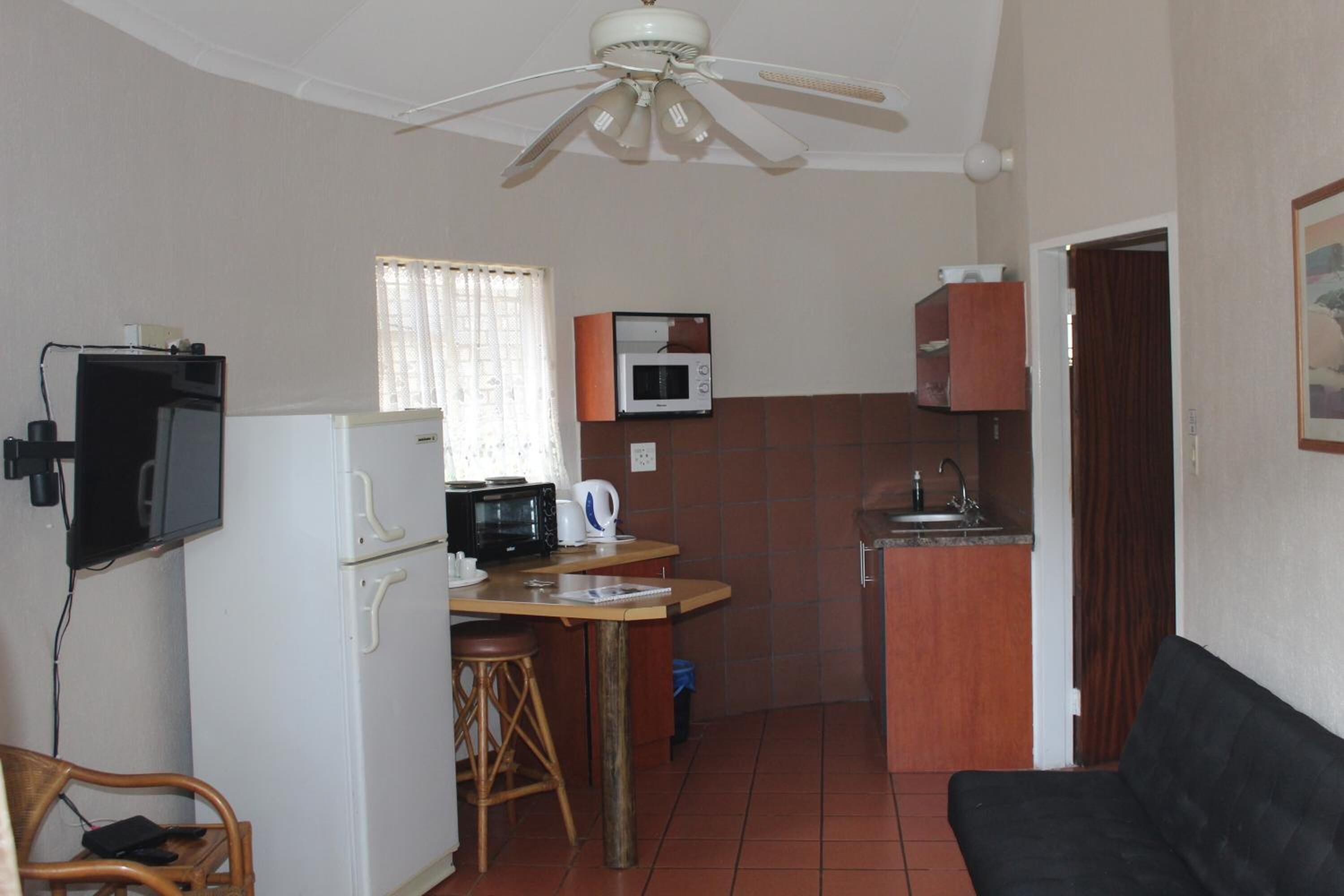 A compact living space with a kitchenette, a ceiling fan, a television, and a sofa.
