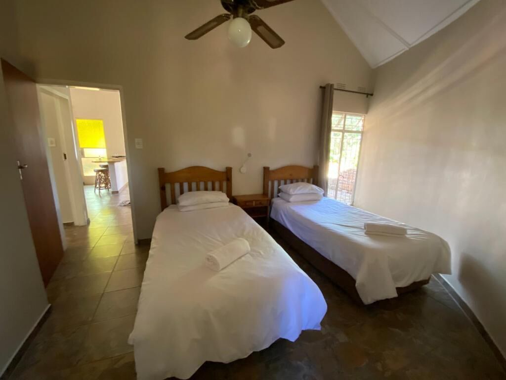 A room with two single beds, a ceiling fan, and a window with curtains.