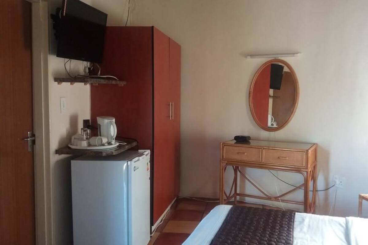 Een slaapkamer met een bed, een kleine tafel, een kledingkast, een televisie en een spiegel.