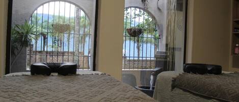 A hotel room with a large arched window, a bed with a patterned bedspread, and a small table with a chair.