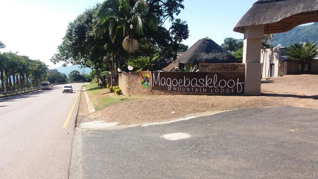 Une route menant au Magooebaskool Mountain Lodge, avec un panneau indicateur et une construction à toit de chaume.