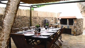 An outdoor dining area with a stone wall, a grill, and a table set for four. - 16 On Main Arniston (Arniston)
