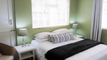 A bedroom with a bed, two bedside tables with lamps, a window with blinds, and a door.
