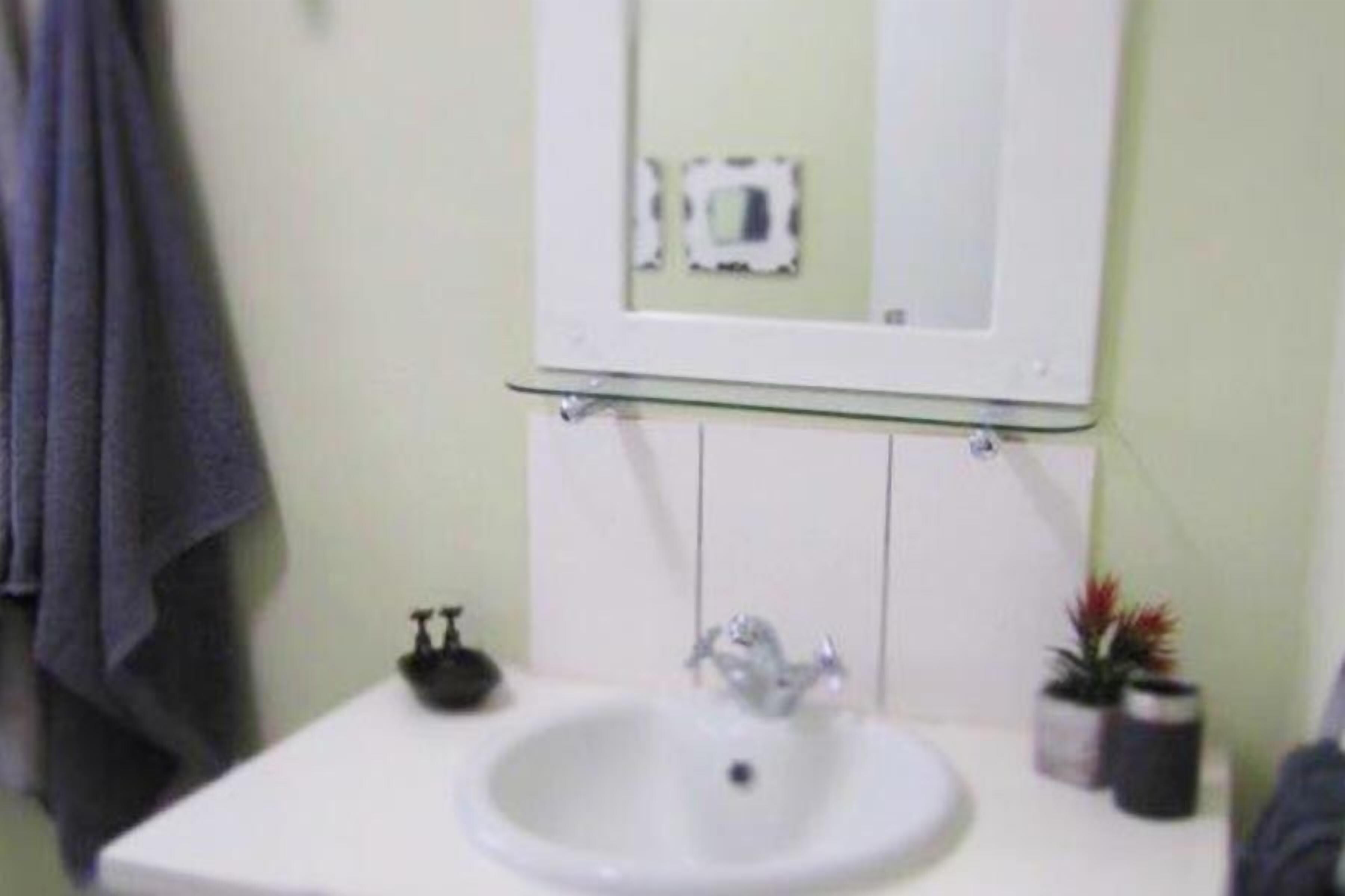 Un baño con lavamanos blanco, un espejo y un perchero para toallas.