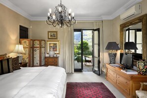 A hotel room with a bed, a TV, a dresser, a chandelier, and a balcony with a view. - 21 Roux Street Guesthouse (Franschhoek)