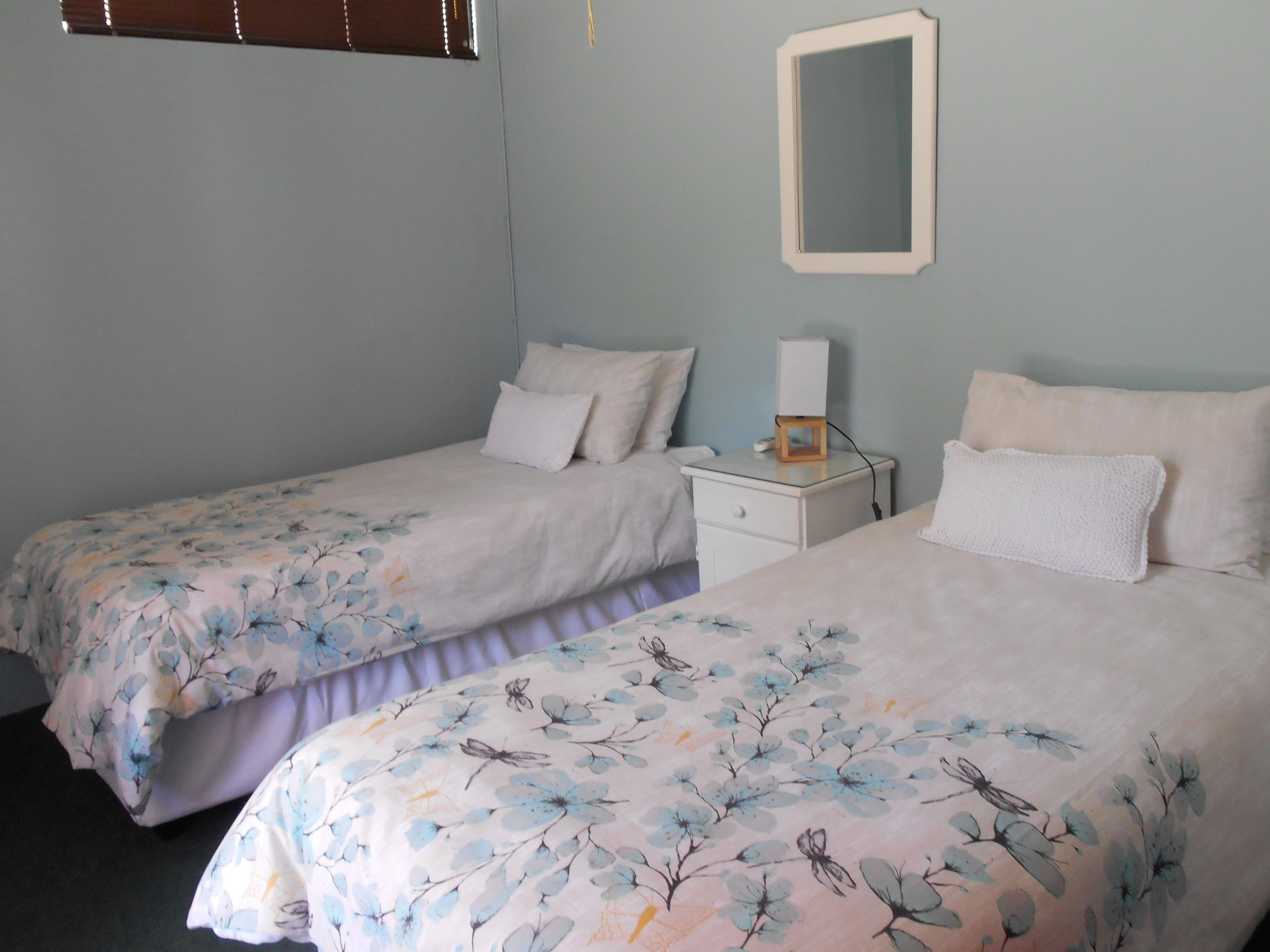 Un dormitorio con dos camas individuales, una mesita de noche con lámpara y un espejo en la pared.