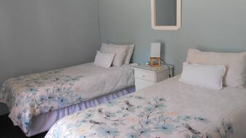 Un dormitorio con dos camas individuales, una mesita de noche con lámpara y un espejo en la pared.