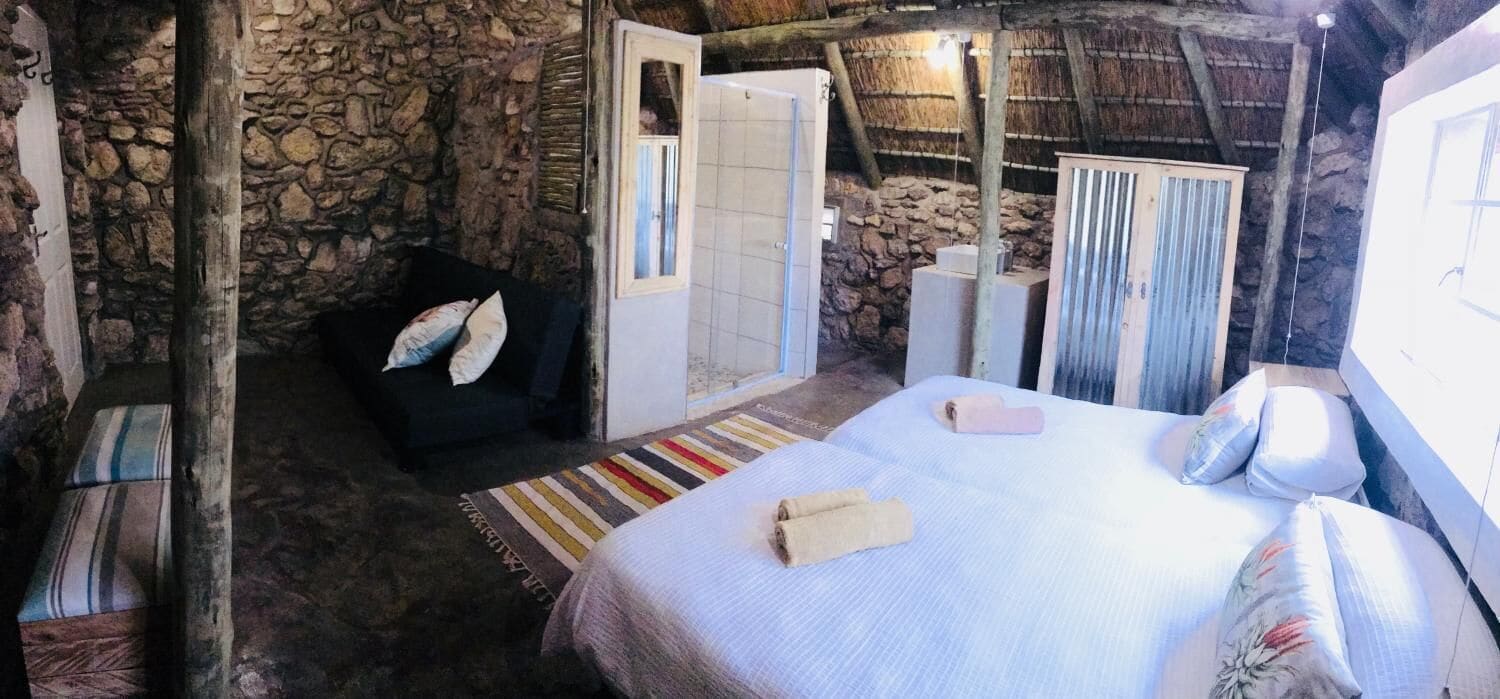 Una habitación rústica con paredes de piedra, una cama con un tapete a rayas, un sofá negro con almohadones y un armario de madera.