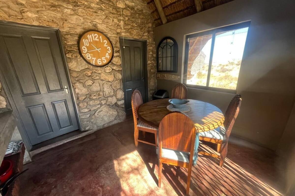 A dining area with a stone wall, wooden table, and chairs. A round clock is on the wall.