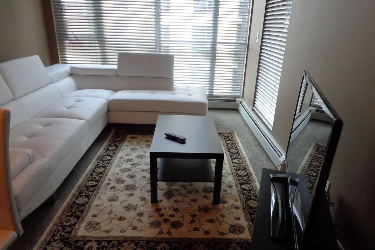 A living room with a white sofa, a small coffee table, and a TV on a stand.